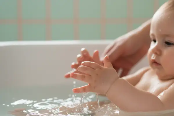 Babyhandjes spelen in warm water in een babybadje tijdens rustig badmoment.